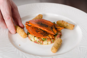 Organic tandoori Mackerel fish fillets, marinated in a vibrant orange tandoori curry sauce, prepared on a white plate with potato, pomegranate and lime wedges.