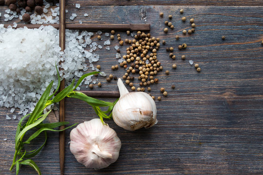 Set of spices to cook fish - white peppercorns, fresh green estragon herb, sea salt, garlic bulbs. Top view. On wooden table. Copy space.