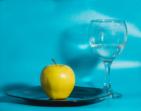 on a blue background yellow Apple in the plate with a glass of water.