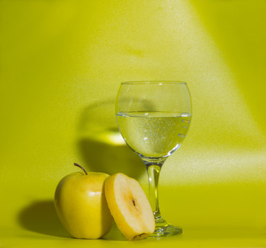 on a green background yellow apples with a glass of water.