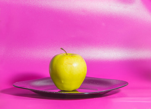 on a pink background on the plate yellow Apple.