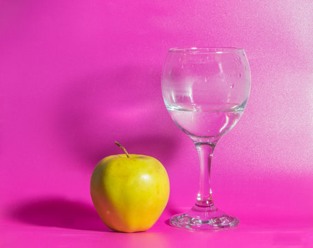 on a pink background yellow Apple with a glass of water.
