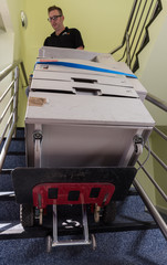 london, england, 02/02/2017 A man in an industrial warehouse lifting heavy items up stairs with a small industrial stair walking lifting style device.