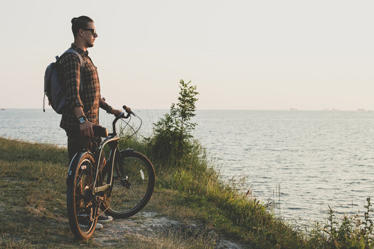 Handsome Young Guy Standing With Bike On Coast And Enjoying View of Nature Sunset Vacation Traveling Relaxation Resting Concept