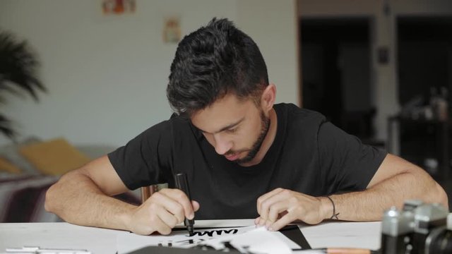 Handsome attractive young artist works in his studio on new project or piece of art, hand lettering a word with thick marker, meticuluously creating new design