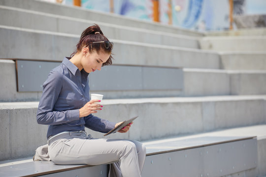 Businesswoman with a tablet  sits on a concrete wall. Online education students