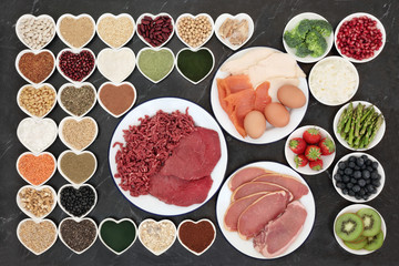 Body building health food with meat, fish, supplement powders, dairy, fruit, vegetables, pulses, nuts, seeds, grains and cereals on porcelain plates.