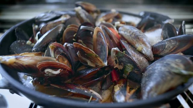 Dramatic zoom into wok pan on top of metal steel gas stove full of steaming vaporized mussels. Delicious mouth watering seafood cuisine in restaurant, freshly made to order