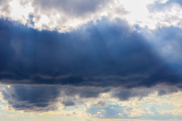 Stormy dark blue sky and sun rays at sunset. Beautiful sky background.