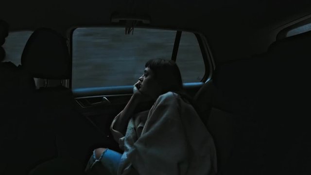 Dark night time shot of young woman sitting in car looking at scenery passing by, tunnels and city lights, moody atmosphere of darkness, she is deep in her thoughts while in taxi
