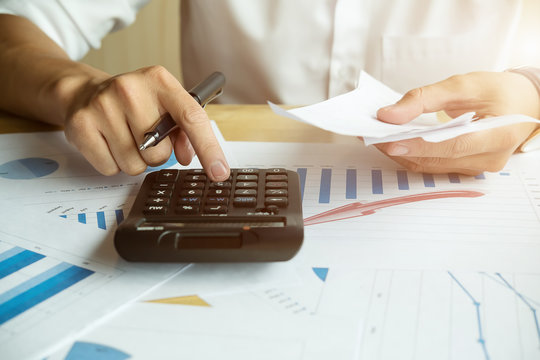 Young man hands holding bills looking at it and using calculator and calculate bills while sitting on desk at home office.