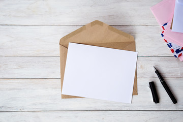 Top view of envelope and blank greeting card with rose flowers on white wooden background.