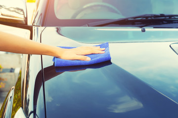 Asian woman's hand wiping surface of car by micro fiber cloth.