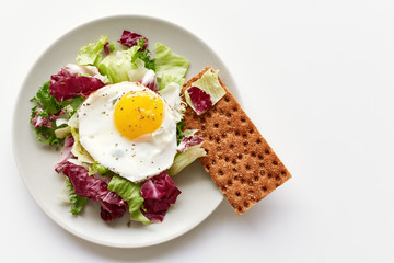 Isolated plate with healthy breakfast containing fried egg, lettuce and crispbread