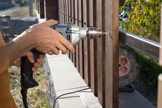 Man hands drilling wooden fence to metal construction. Building a wooden fence with a drill and screw. Close up of his hand and the tool in a DIY concept.