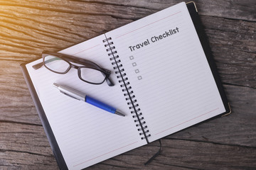 Conceptual,notebook on a wooden table. open diary, glasses and pen with Travel Checklist word.