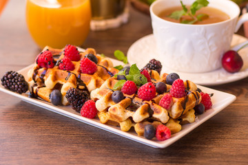 Belgium waffles with raspberries, chocolate and syrup on a plate.