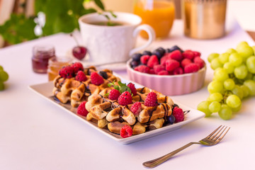 Belgium waffles with raspberries, chocolate and syrup on a plate.