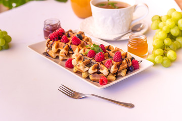 Belgium waffles with raspberries, chocolate and syrup on a plate.