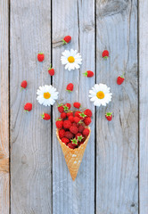 Ripe fresh raspberries and white chamomile flowers in ice cream cone on rustic wooden background. Stylish flat lay. Minimal and creative concept.