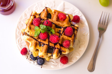 Belgium waffles with raspberries, chocolate and syrup on a plate.