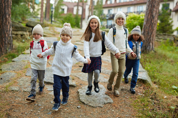 Group of cheerful children running towards camera holding hands on their first school day in September