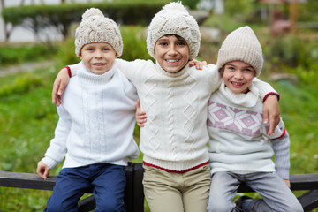 Three happy boys playing outdoors in countryside, posing to camera sitting on wooden fence and smiling  enjoying warm autumn day