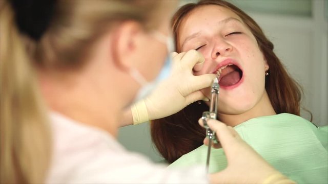 Anesthetic injection in dental cabinet. Female dentist doing injection to girl patient. Selective focus