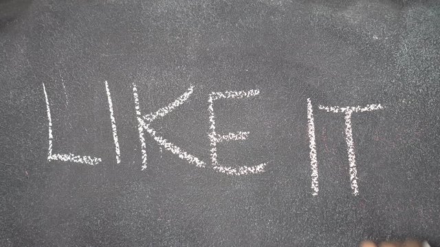 Woman's hand writing "LIKE IT" with white chalk on blackboard