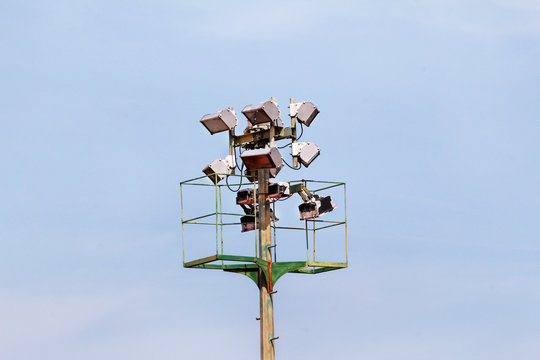 Stadium floodlight tower with reflectors with blue sky. Lighting pole tower at the sports stadium and ground. Big lamp and light stadium poles or sports lighting. Flood light pole in the spotlight.