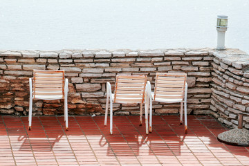 White chairs on a balcony. Traditional mediterranean seaside and rest time on terrace white old chairs and amazing blue sea. Empty chairs are looking toward the sea, surrounded by stone wall.