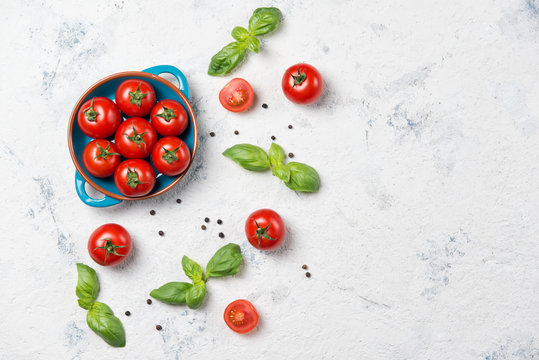 Fresh cherry tomatoes on a plate, basil leaves and black pepper on stone table, top view
