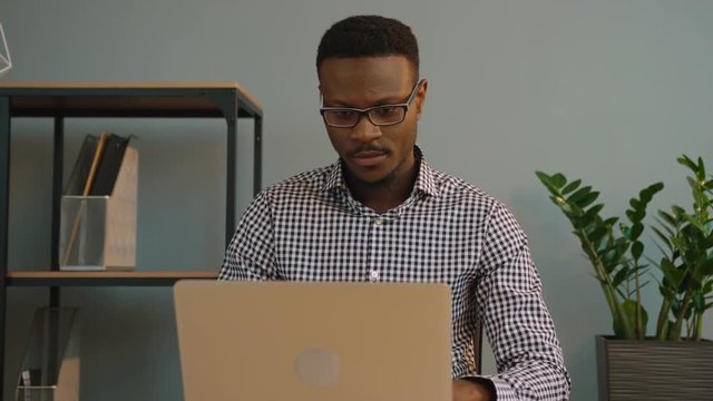 African american business man using laptop computer at the office. Black office worker looking at the screen monitor and writing something in notebook. Close up