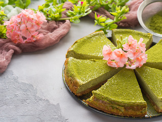 Matcha baked cheese cake and pink flowers on gray concrete background