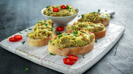 Homemade Guacamole toast with chili pepper, parsley on white wooden board