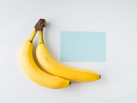 Two bananas on white background. Minimal flat lay with empty blue paper card