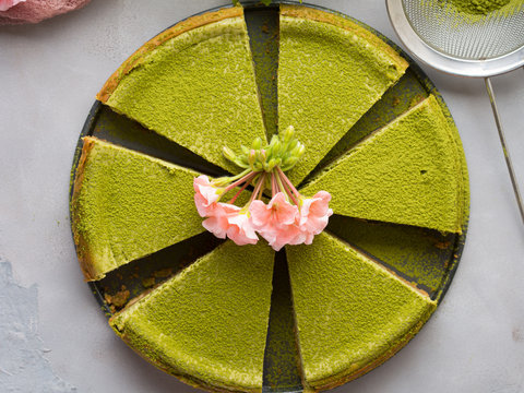 Matcha baked cheese cake and pink flowers on gray concrete background