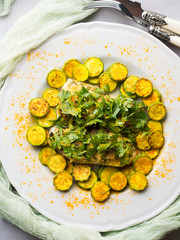 Baked Stock fish fillet with almond parsley topping and turmeric courgettes on white plate. Healthy diet dish