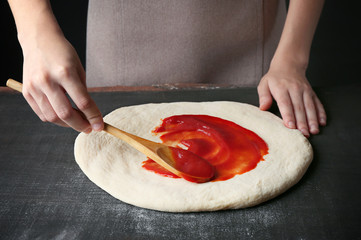 Female hands making traditional pizza on black table, close up