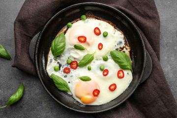 Delicious over hard eggs with green peas, pepper and basil leaves in pan on kitchen table