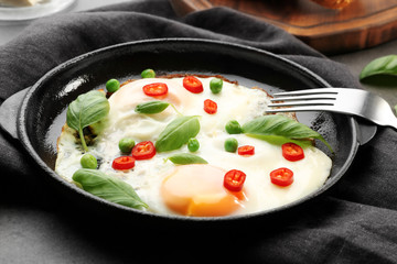 Delicious over hard eggs with green peas, pepper and basil leaves in pan on kitchen table