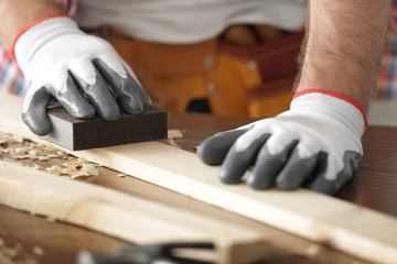Carpenter sanding wooden plank on table, closeup
