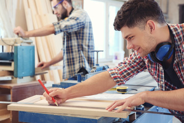 Carpenter applying marking onto wooden board in workshop