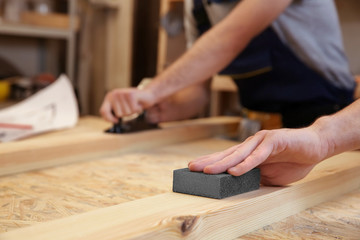 Fototapeta na wymiar Hand of carpenter machining wooden board with abrasive stone, closeup
