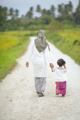 Obraz premium Mom holding her baby girl hand with hari raya dress