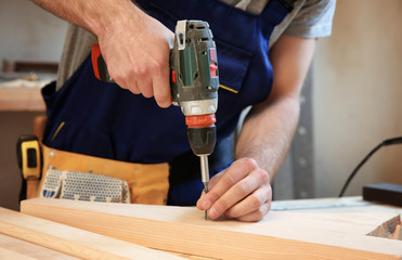 Carpenter driving screw nail into wooden board in workshop, closeup
