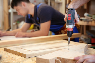 Carpenter driving screw nail into wooden board in workshop, closeup