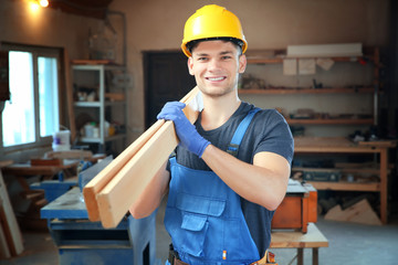 Handsome young carpenter with boards in workshop