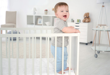 Cute little baby standing in crib at home