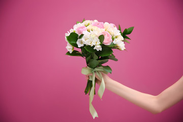 Female hand holding beautiful bouquet with white freesia on color background